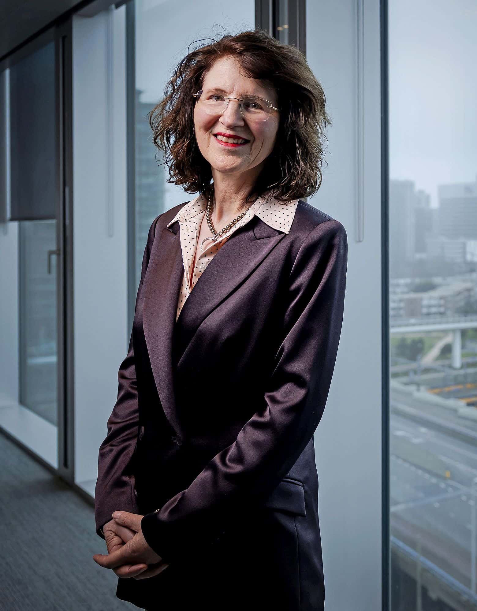 Staatssecretaris Annet Bertram staat voor een raam van haar ministerie met uitzicht op station Den Haag Centraal.