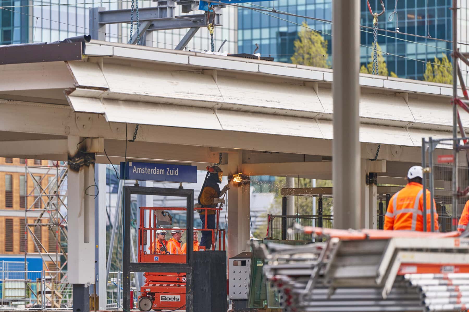 Een man in oranje overal zaagt met een slijptol een balk weg die de oude overkapping van het perron ondersteunt.